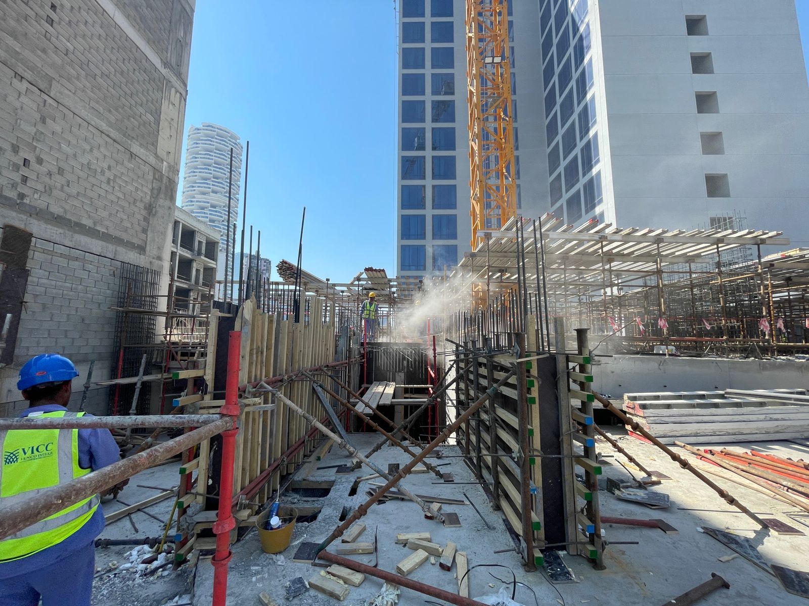 Pearl House By Imtiaz Construction site with scaffolding, workers, and cranes under a clear blue sky. Building materials are scattered around.